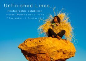 Poster for “Unfinished Lines” photography exhibition, showing a person seated on a yellow rock against a blue sky.