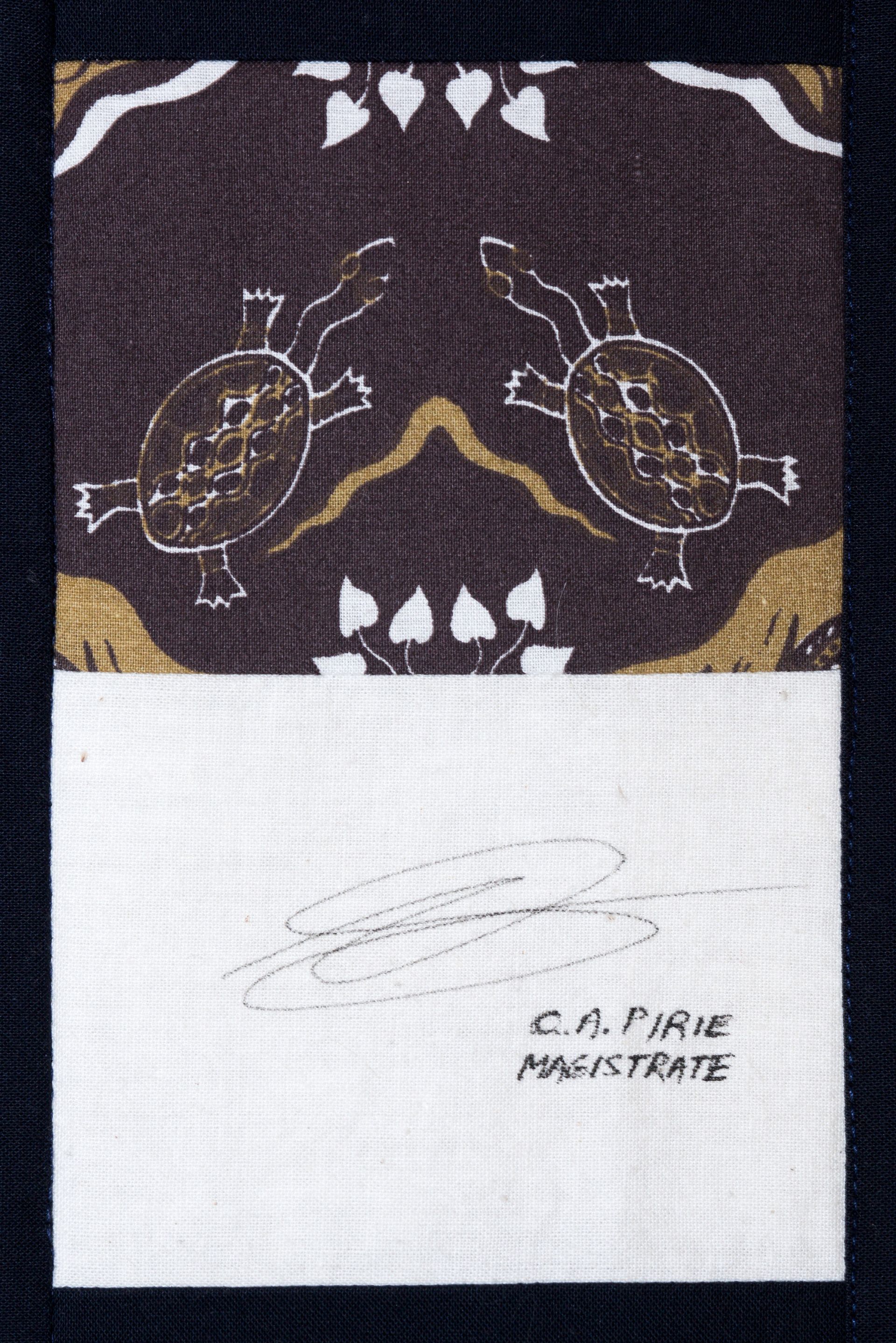 Dark woven textile with two turtle motifs above a white panel and handwritten signature at bottom right