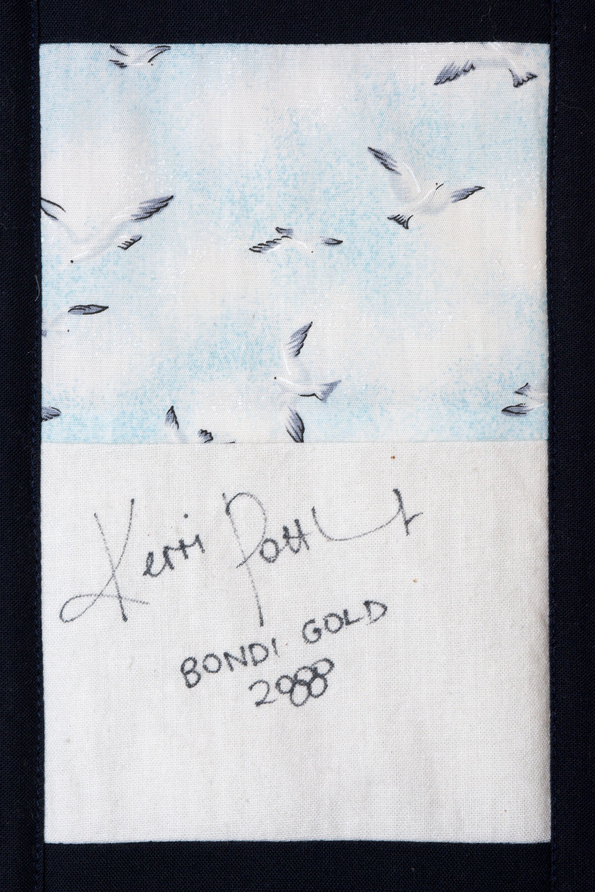 White fabric with scattered small dark fish-like shapes and handwritten text reading “BONDI GOLD 2008.”