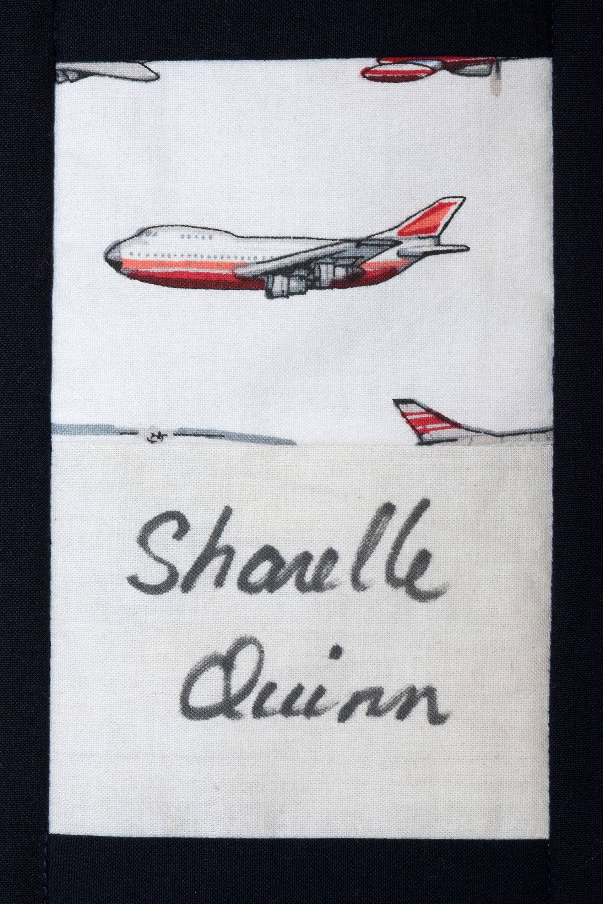 White label with red airplane illustrations and handwritten name “Shaullie Quinn”.