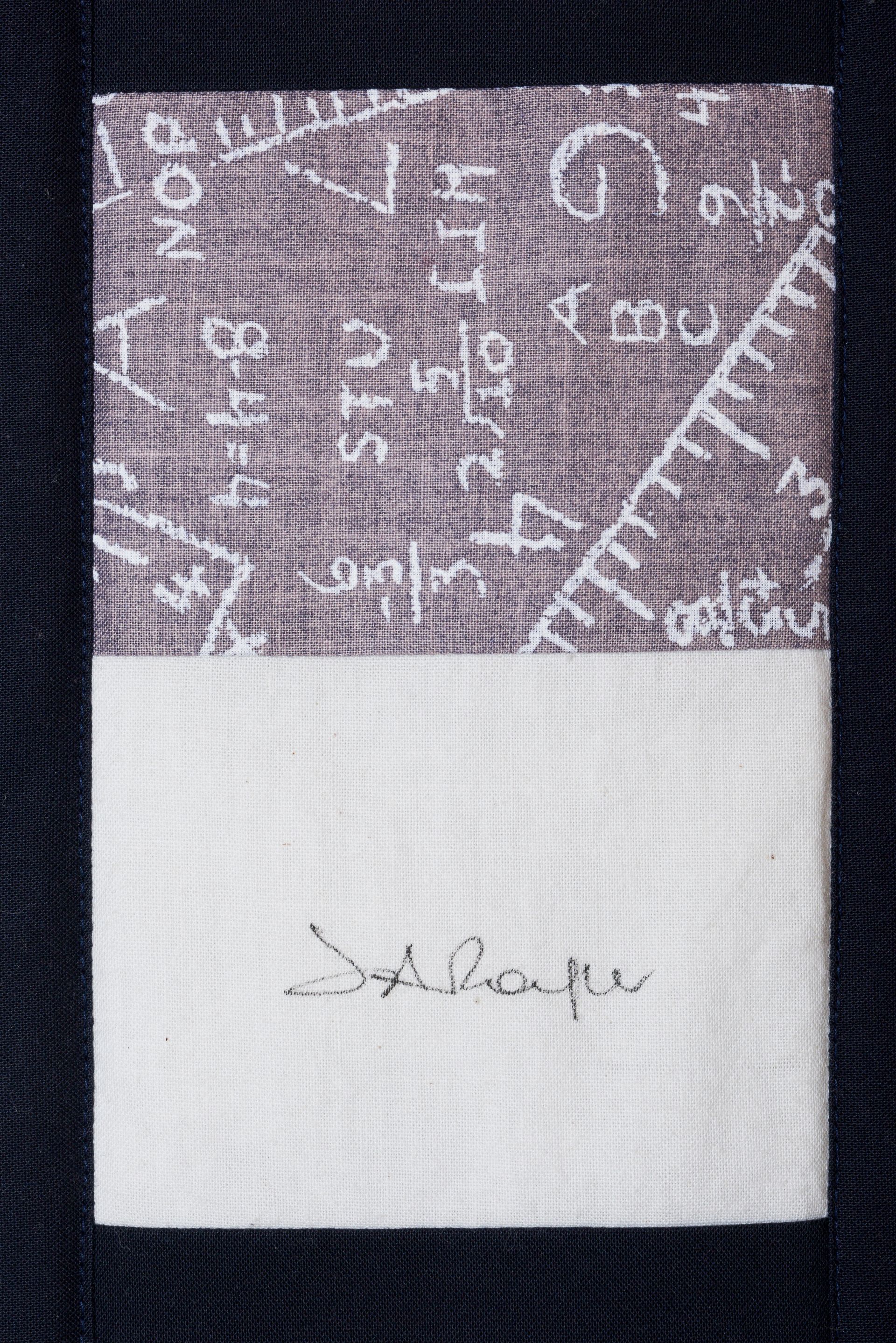 Folded gray patterned fabric with a white lower section and small handwritten text in the center