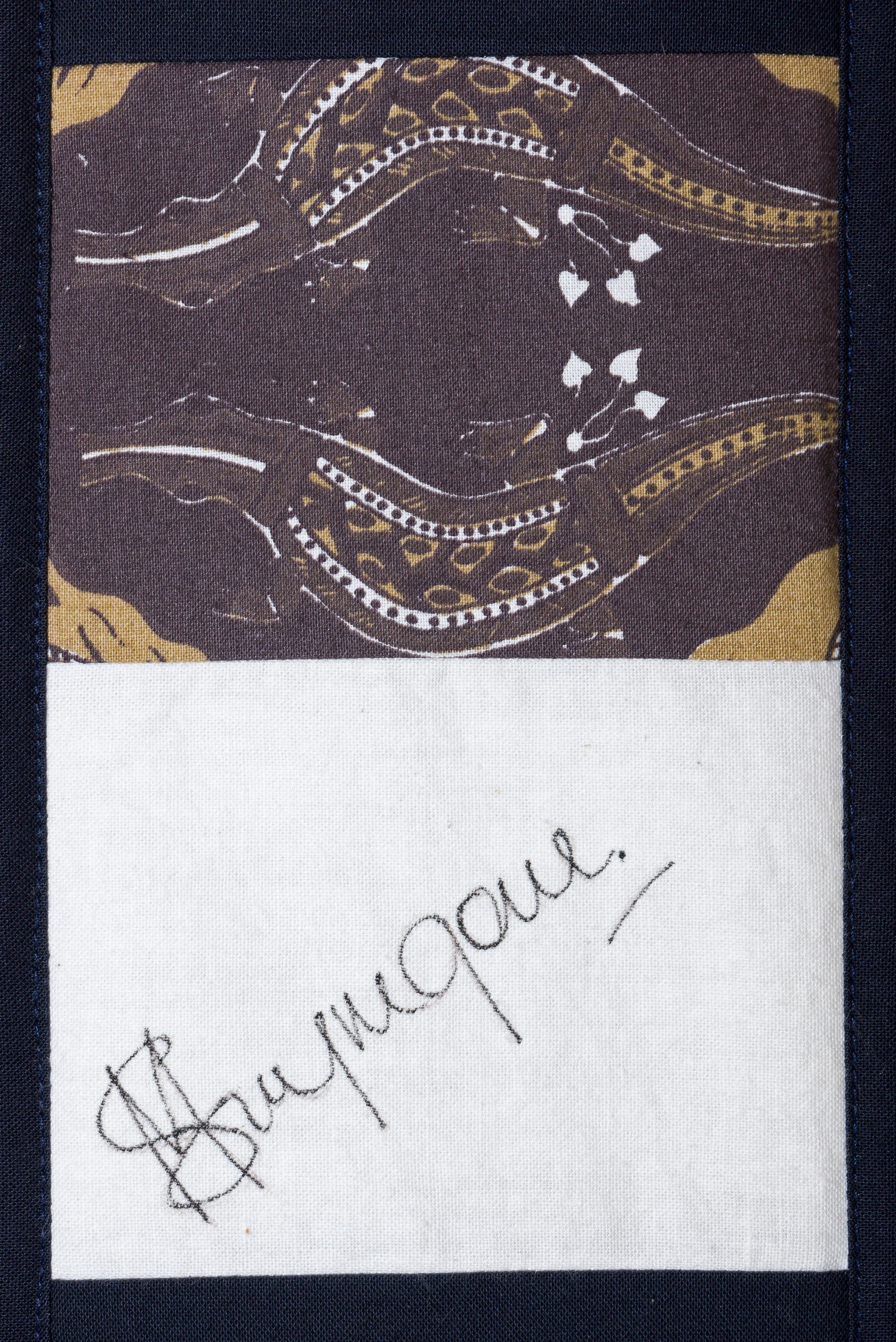 Close-up of a patterned fabric with a white panel and handwritten signature stitched below it.
