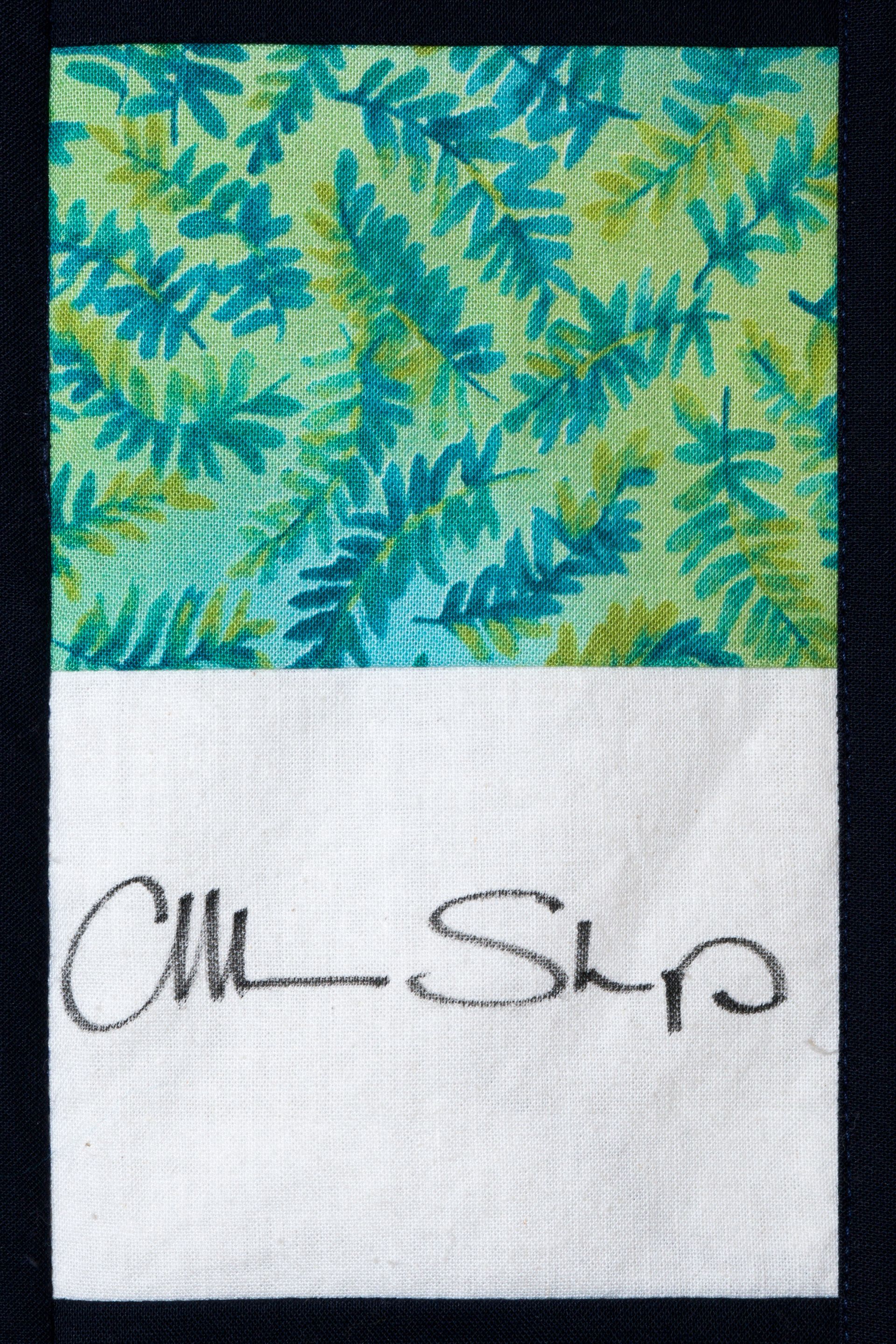 Green and blue leafy fabric above a white label with a handwritten signature