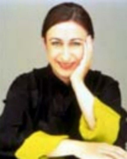 Smiling person in a black top with yellow sleeves, resting their head on one hand at a table.