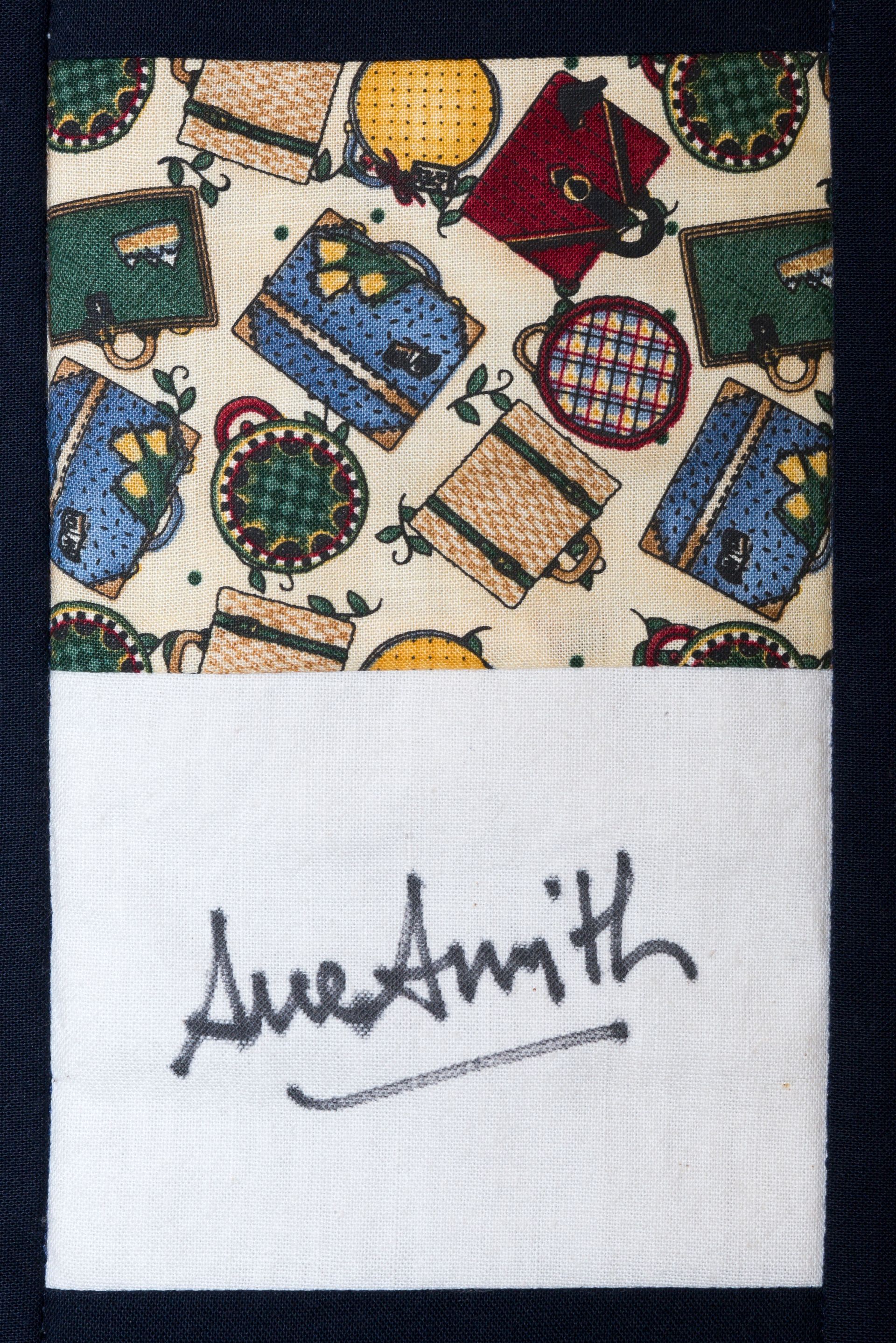 Patterned fabric with colorful suitcase motifs above a white label reading “Aue Smith”