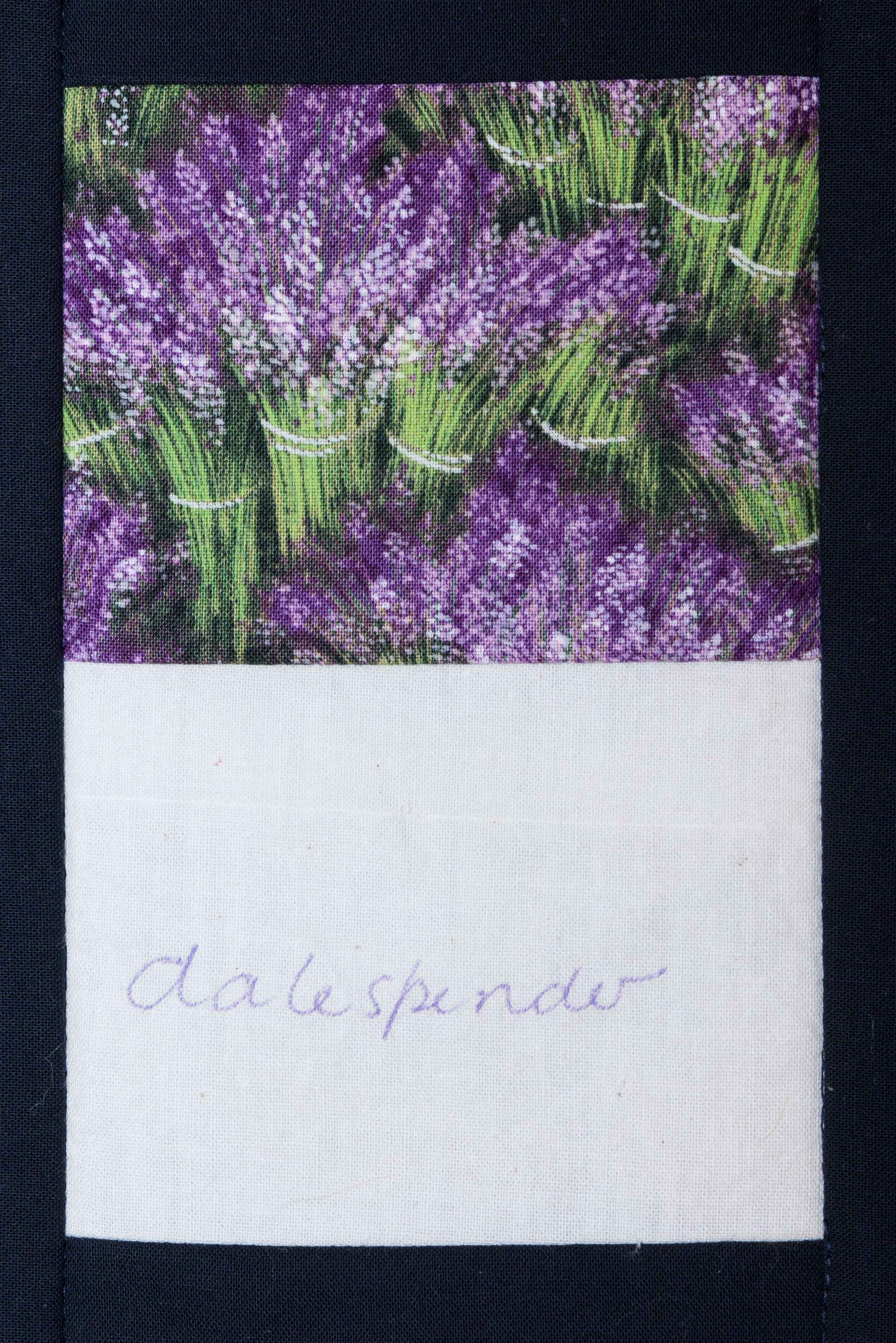 Purple flowers above a white handwritten label on a dark woven background