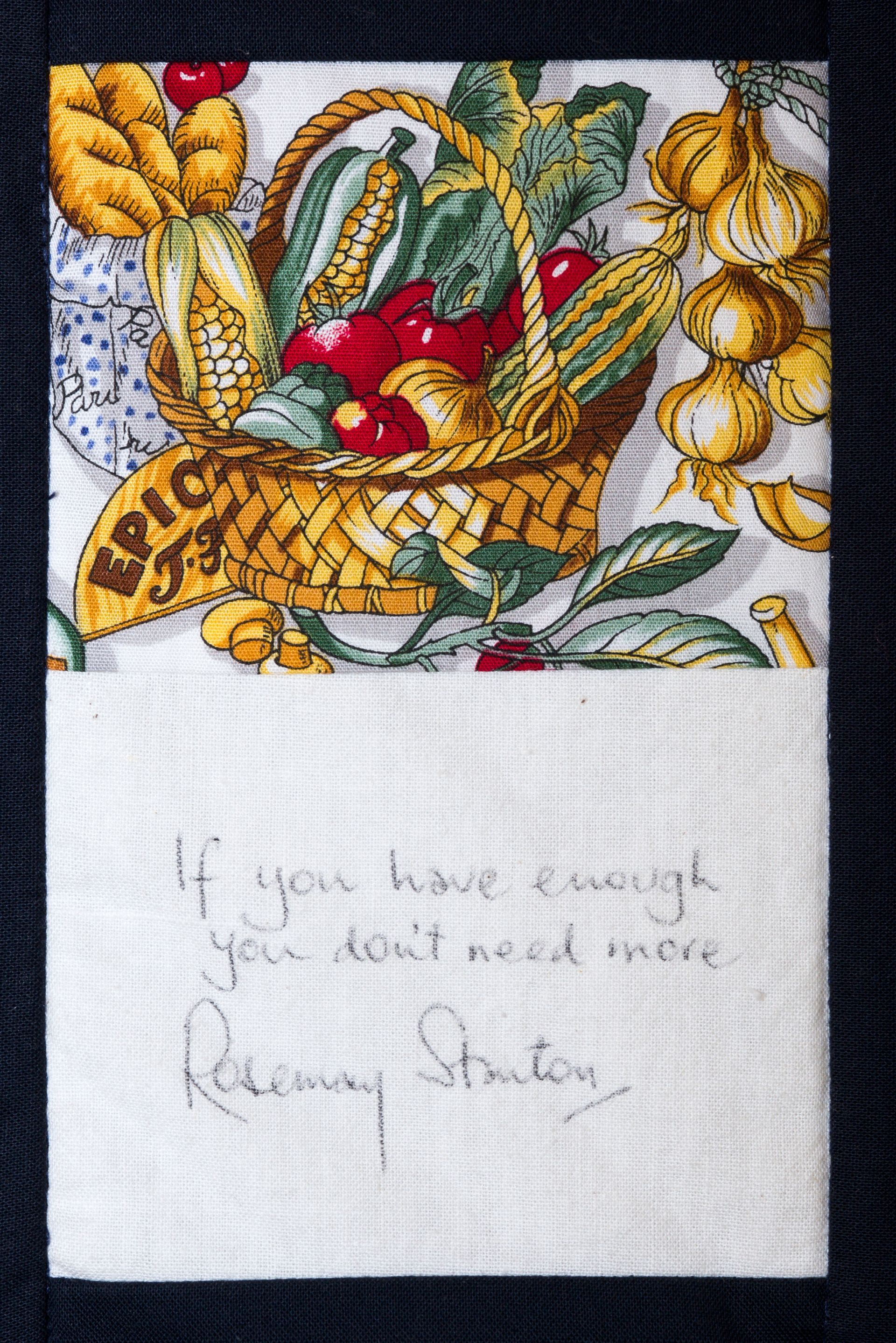 Embroidery of a fruit basket with bananas, pears, and grapes above a handwritten note on white fabric