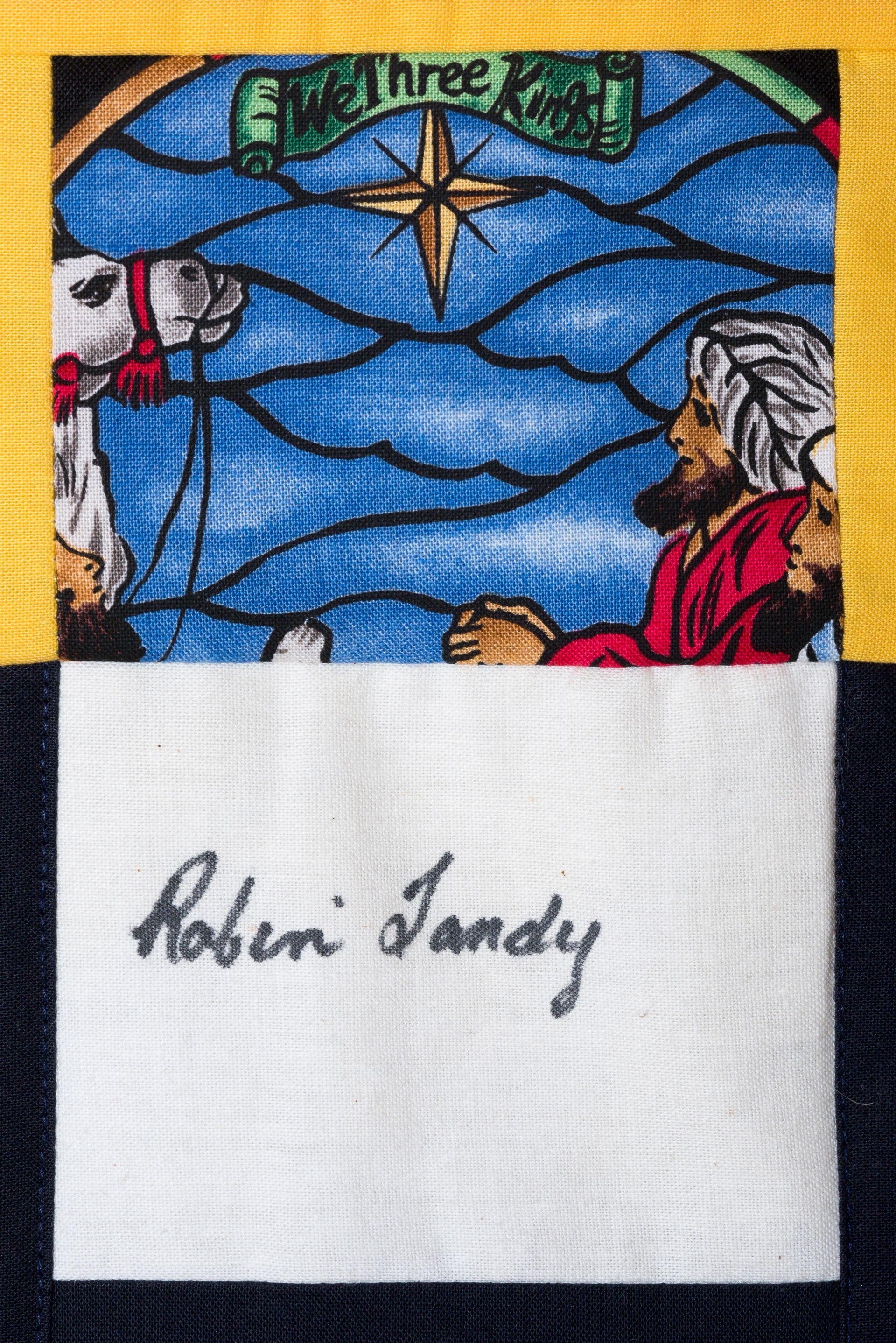 Blue stained-glass panel with a star and figures above a white card signed “Robin Sandy”