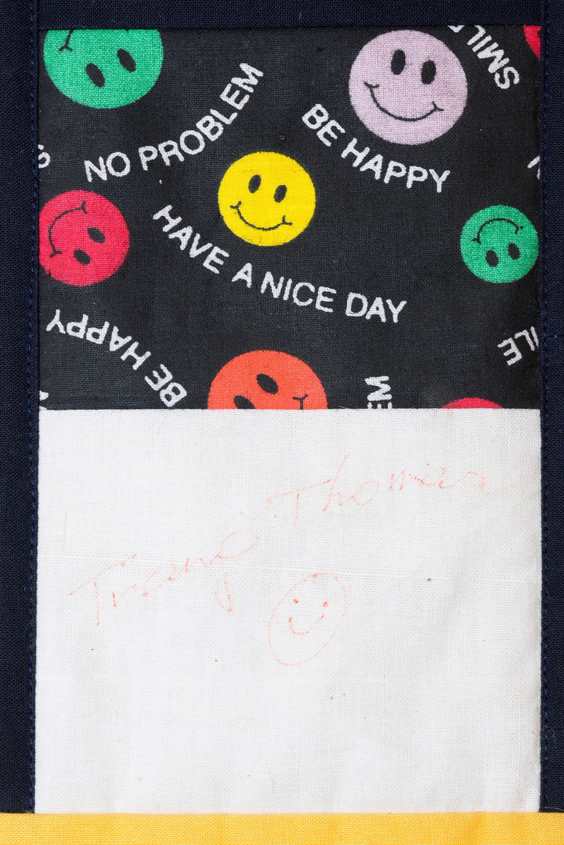 Black cloth with colorful smiley faces and “Have a nice day” text above a blank white label area.