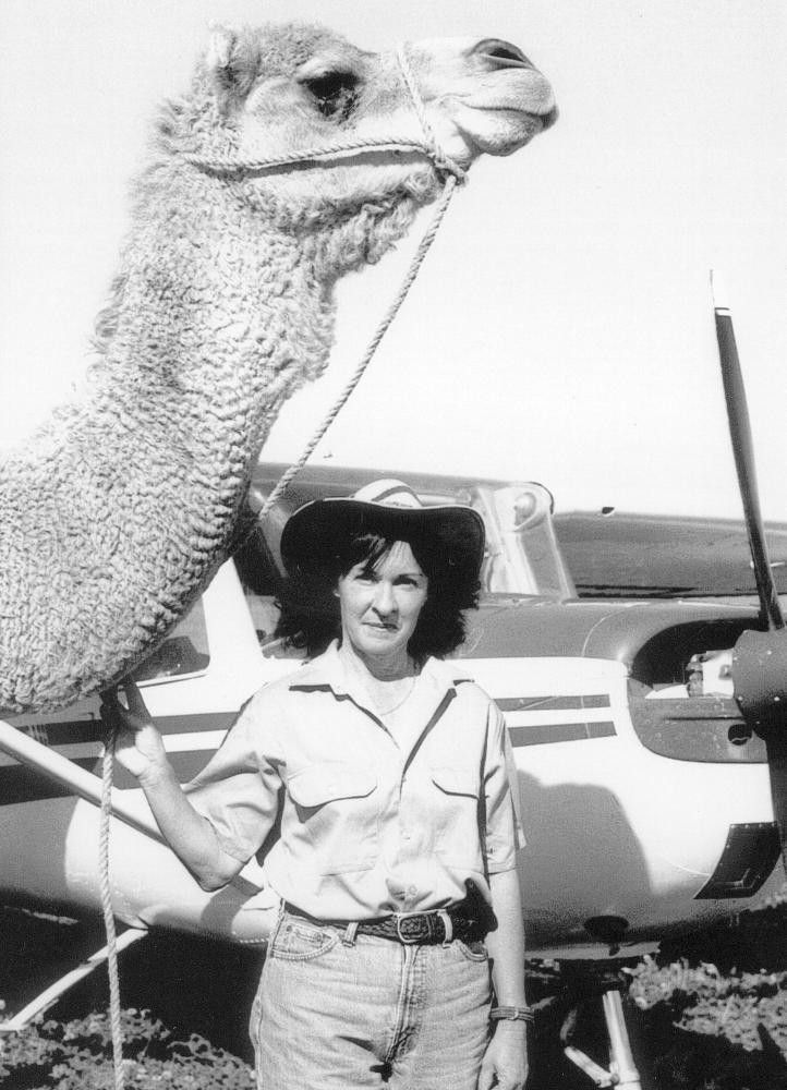 Woman standing beside a camel near a small airplane outdoors