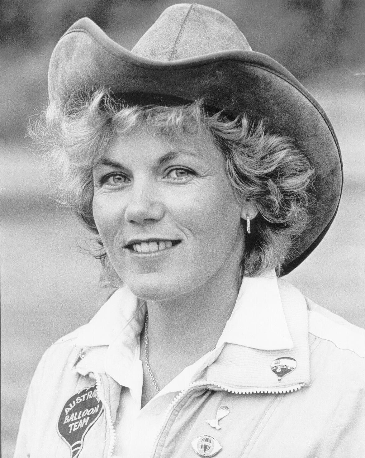 Black-and-white portrait of a smiling person in a cowboy hat and Western shirt with pins