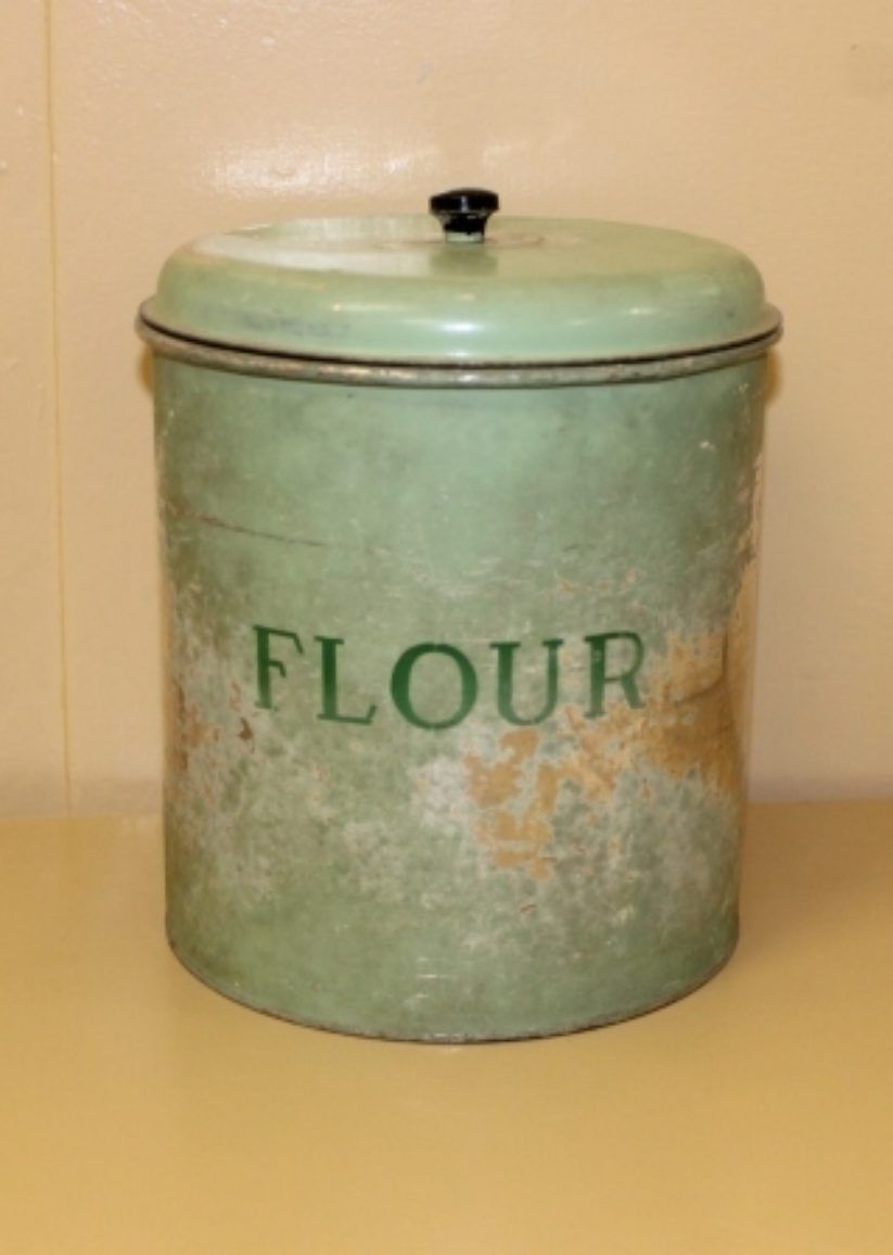 Vintage green flour canister on a beige surface, labeled “FLOUR.”