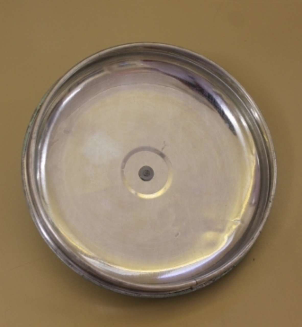 Round stainless steel lid with a small central hole on a tan background