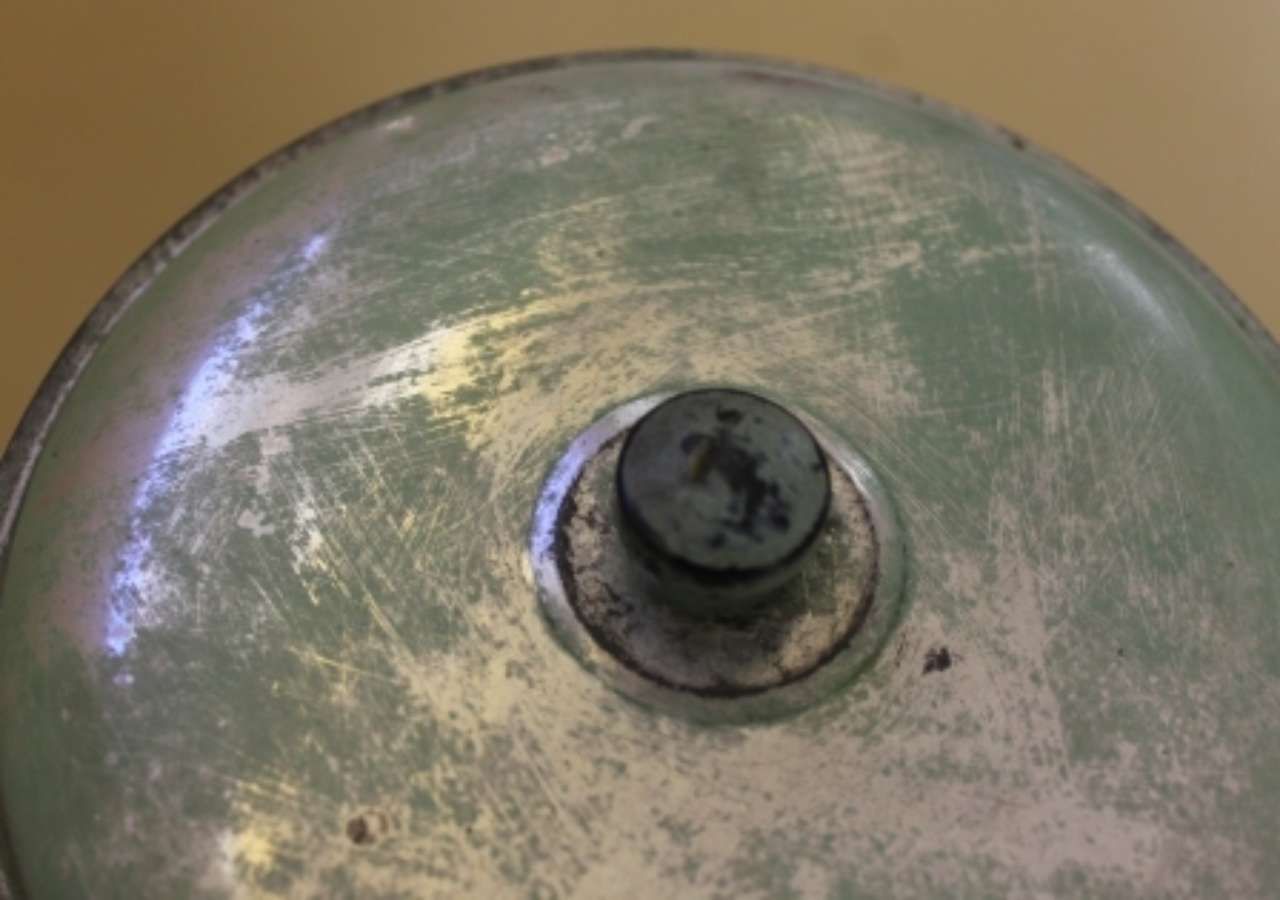 Close-up of a worn green metal pot lid with a black knob handle