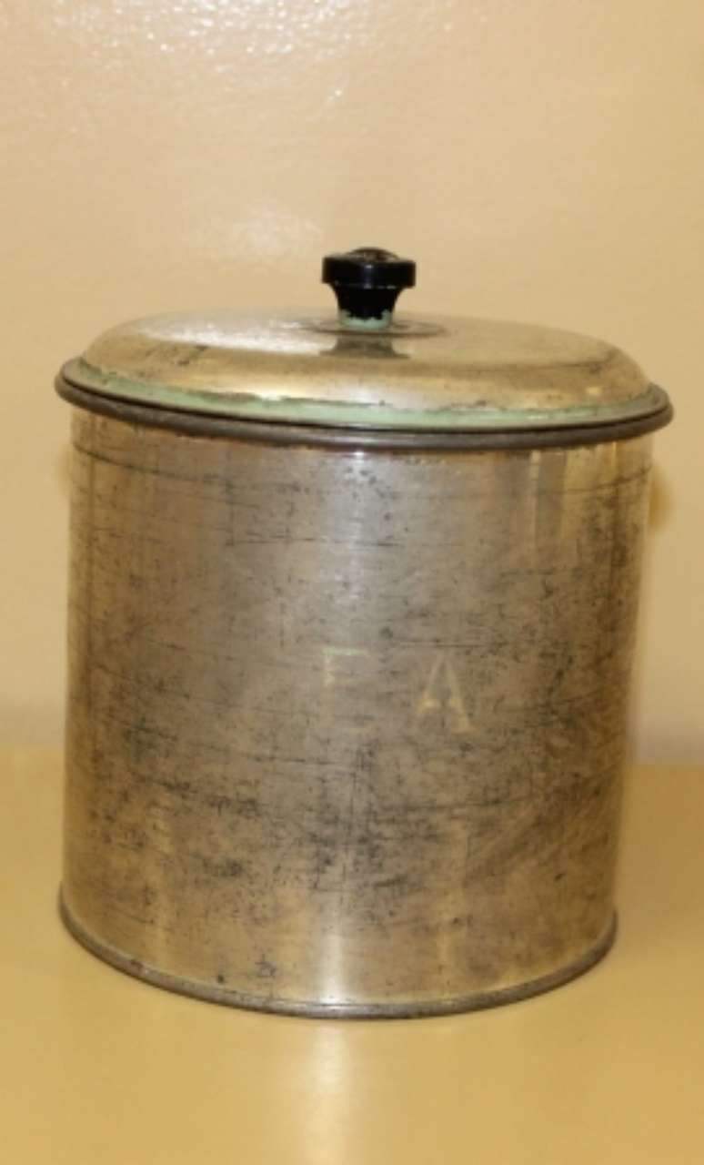 Small silver metal canister with a lid and black knob on a plain beige surface.