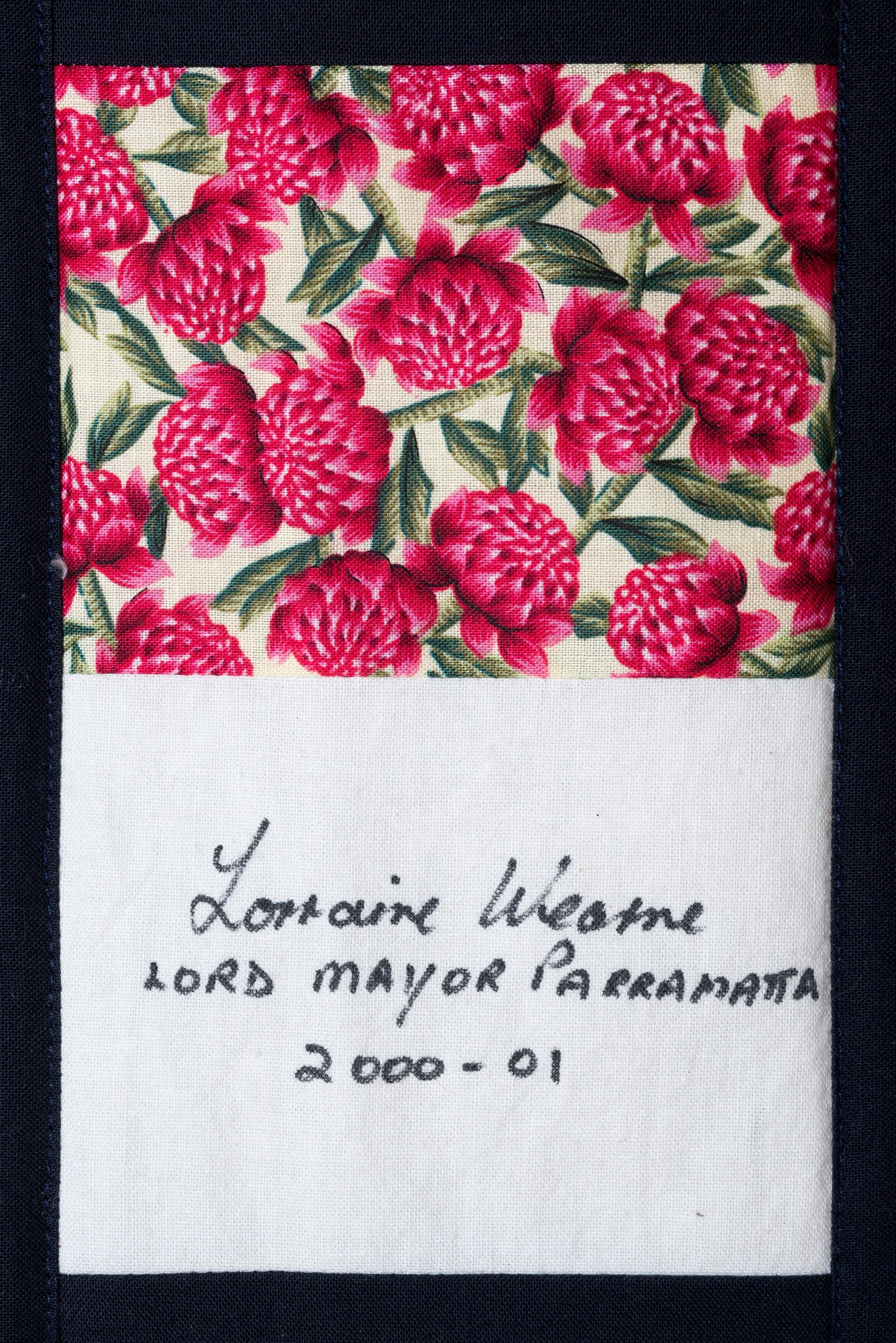 Fabric swatch with pink floral print and handwritten name and date on white cloth: “Loriah Nierne, 2000-01”