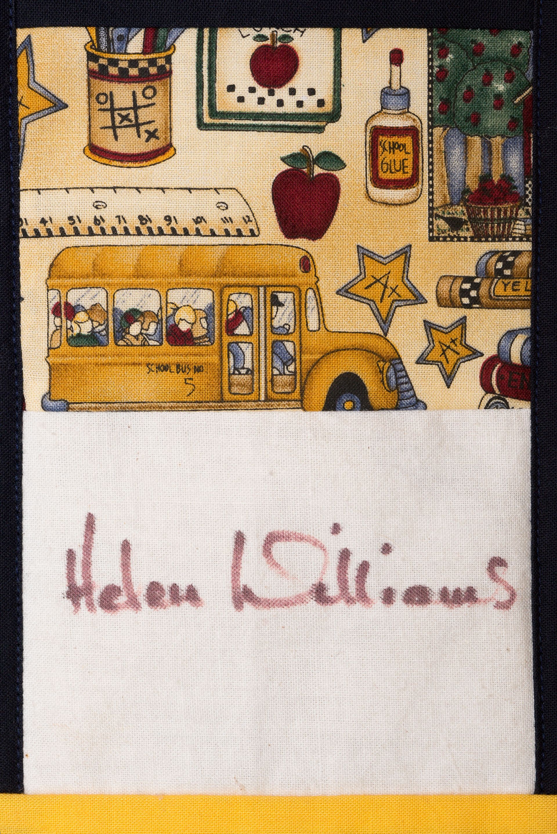 Handwritten name on white cloth beneath a colorful illustrated school bus