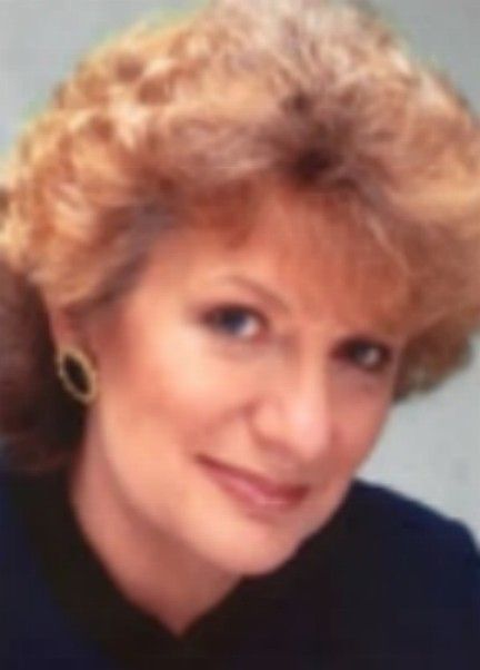 Portrait of a smiling woman with short curly blonde hair against a plain background