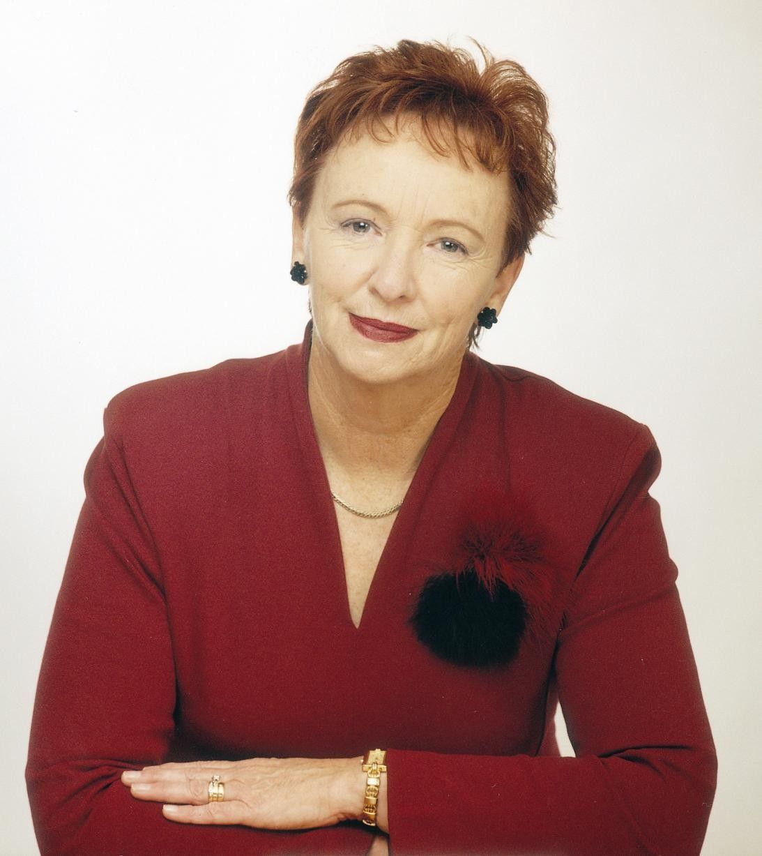 Portrait of a woman in a red blazer, seated against a white background.