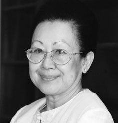 Black-and-white portrait of a smiling person wearing round glasses and a light top