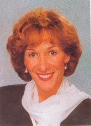 Smiling woman with short curly hair, wearing a white scarf on a gray background