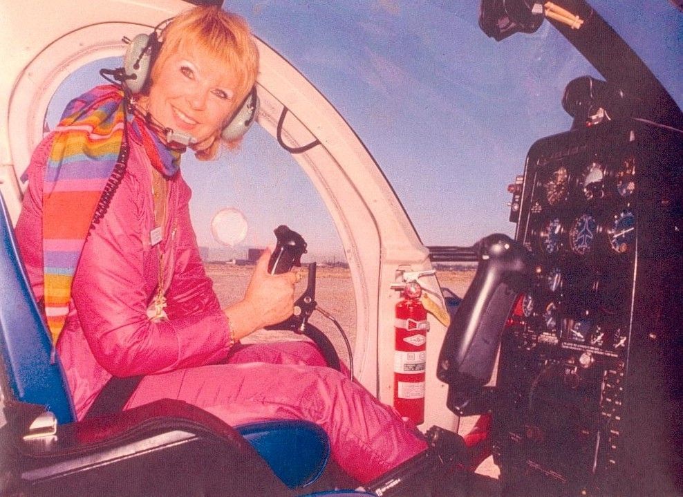 Person in a pink racing suit sitting in a cockpit, smiling and holding a control lever.
