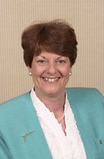 Smiling woman in a turquoise jacket and white blouse against a beige background