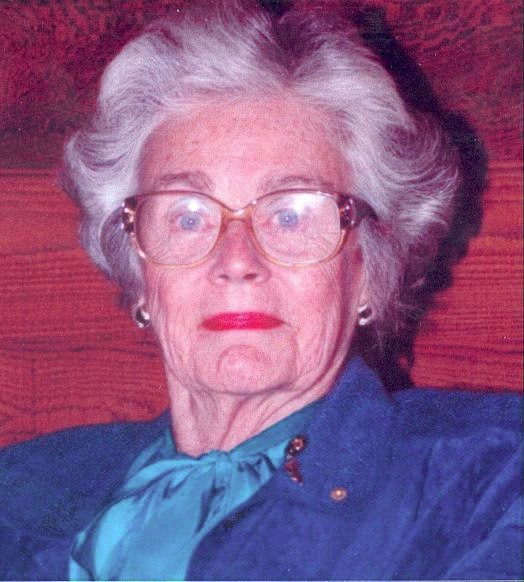 Portrait of a woman with white hair, glasses, and a blue blouse against a red background