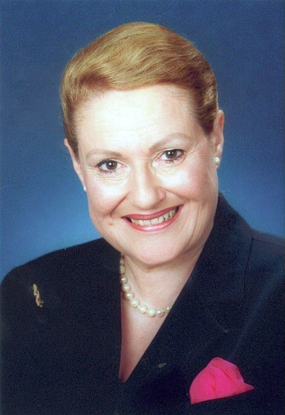 Smiling woman in a dark blazer with a pink pocket square against a blue background