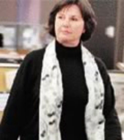 Woman in a black turtleneck and white patterned scarf standing indoors.