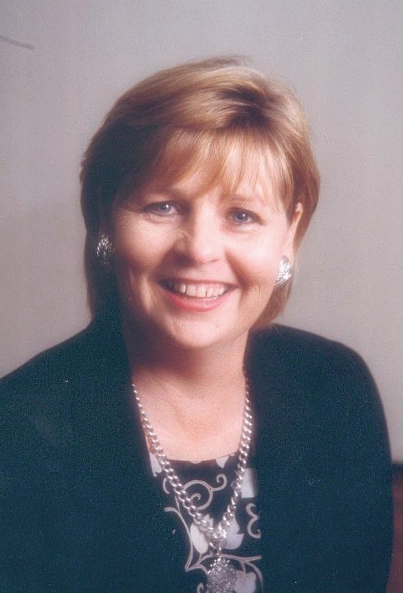 Smiling woman in a dark blazer and patterned top against a soft gray studio background