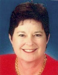 Smiling woman with short dark hair, wearing a red top and gold necklace against a blue background