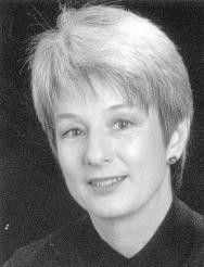 Black-and-white portrait of a smiling person with short light hair against a dark background