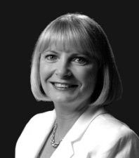 Black-and-white studio portrait of a smiling woman in a light blazer