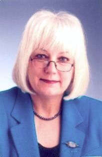Portrait of a woman with blonde hair and glasses wearing a blue blazer against a light background