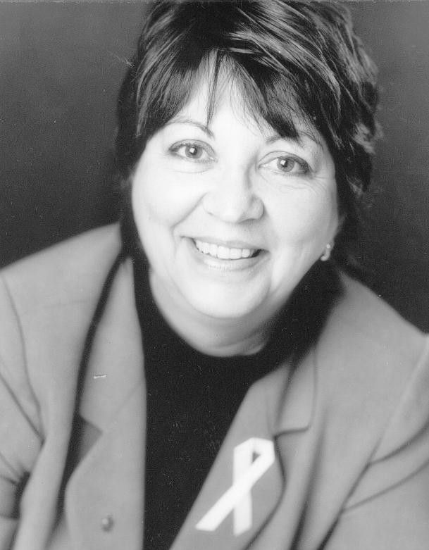 Smiling woman in a blazer with a white awareness ribbon pin.
