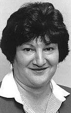 Black-and-white headshot of a person in a collared shirt and jacket, smiling slightly.