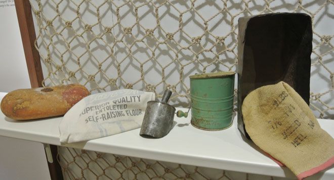 Assorted bread rolls and cans displayed on a white shelf, with a dark backdrop and netted wall behind.
