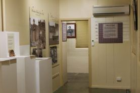 Narrow beige hallway with framed photos, white cabinets, and a wall-mounted air conditioner.