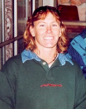 Smiling person in a green sweater and blue collared shirt indoors by a window