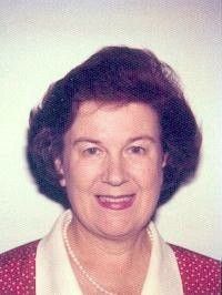Portrait of a smiling woman with dark hair, wearing a red jacket and pearl necklace on a light background