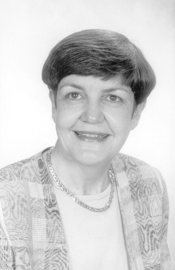 Portrait of a smiling person in a patterned jacket and necklace against a plain background