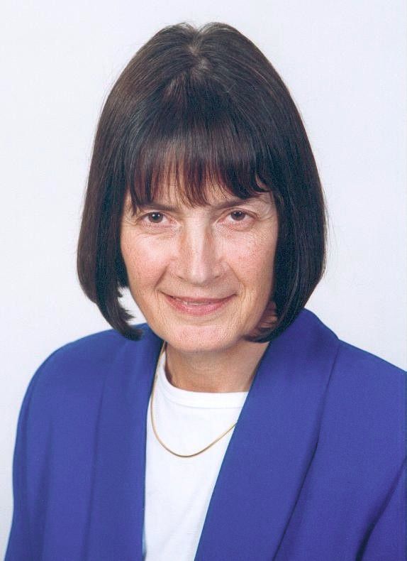 Portrait of a woman with a dark bob haircut, wearing a blue blazer and white top, against a plain background