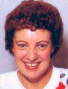 Smiling woman with short curly brown hair against a plain background