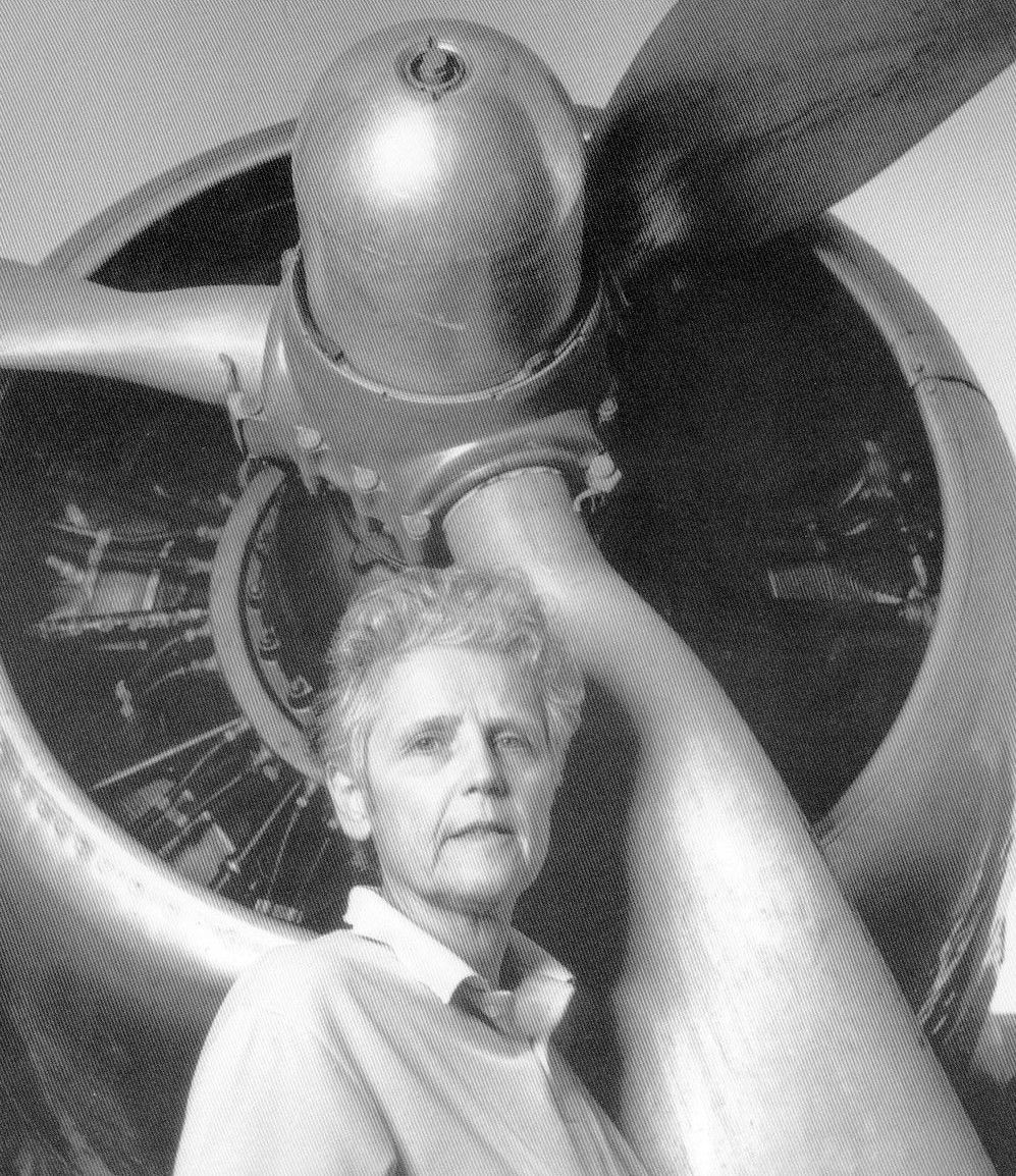 Person standing before a large airplane propeller engine, looking toward the camera.