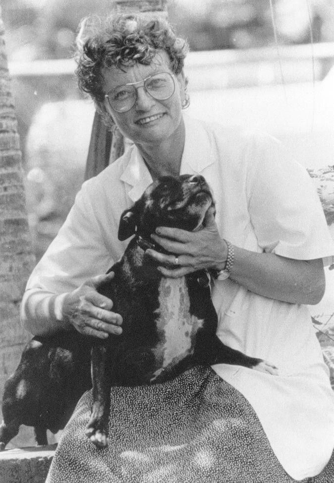 Smiling person in a white shirt holding a black-and-white dog outdoors