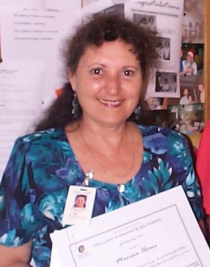 Woman holding a certificate and ID badge, smiling indoors against a bulletin board backdrop