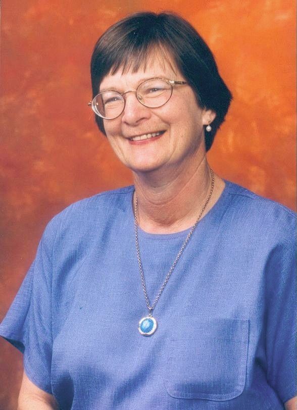 Smiling woman in glasses wearing a blue top and pendant against an orange backdrop