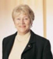 Portrait of a person in a black blazer and cream turtleneck, standing against a light background