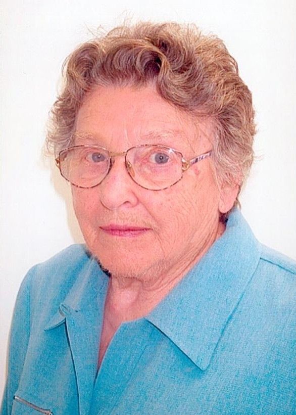 Portrait of a woman with glasses and short curly hair wearing a blue blouse against a white background